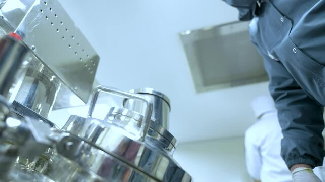 pharma worker using pharmaceutical large machines making medicines in cleanroom stainless steel equipment with pharma grade machinery boxes in a pharmaceutical factory for manufacturing. ppe kit suit