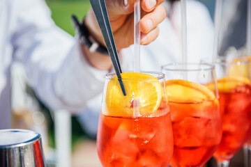 The bartender's hand adds a slice of lemon to a red cocktail with ice using tweezers. Creating the popular cocktail Aperol Spriz close-up. Refreshing cocktail in summer. Beach bar, cold drinks