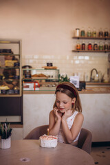 A child girl in a cafe at a table with a cake on the day of the holiday is happy and sweet