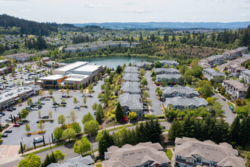 Aerial drone view of Beaverton, Oregon, featuring Progress Lake Park, residential neighborhoods, shopping centers, and parking lots, with tree-lined streets and a mix of suburban and commercial spaces