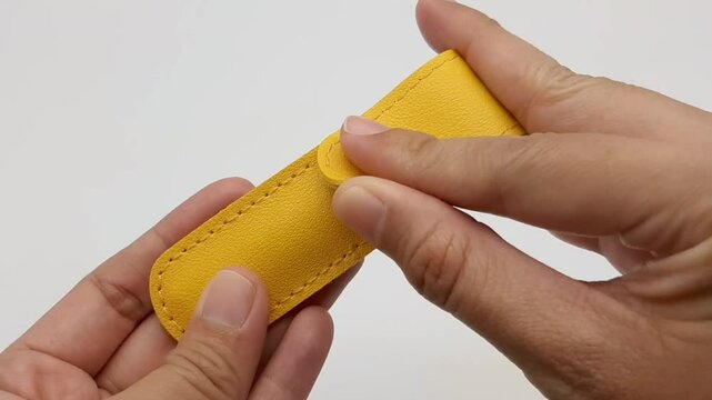 Both hands are opening a yellow leather case for the ear pick set.