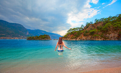 Young happy and playful red hair woman in blue bikini swimming on the turquoise sea playing with waves enjoying summer holidays Ölüdeniz beach And Blue Lagoon - Oludeniz, Fethiye, Turkey