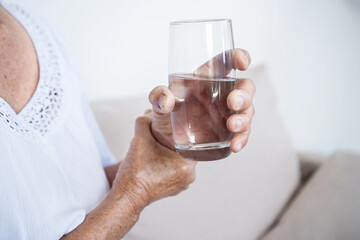 Elderly woman with Parkinson's disease struggling to drink water from a glass due to uncontrollable...