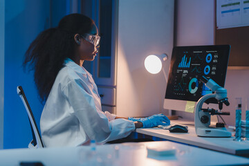 Young female scientist wearing lab coat and protective glasses analyzing charts and graphs on...