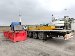 A truck with a trailer at the plant site awaits the loading of red skips filled with drilling mud and oil waste.