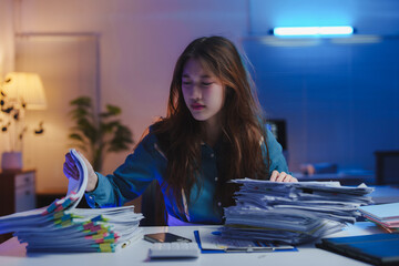 Young business woman working overtime in office at night, checking accounting documents, preparing paperwork using calculator and laptop, focused employee working hard analyzing financial reports