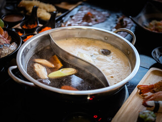 Close-up photo of a stainless steel hot pot divided into two parts, with two different types of soup: a dark, rich soup on one side and a light, clear soup on the other.