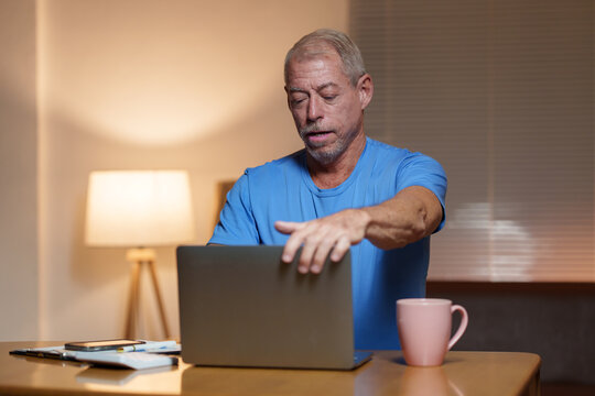 Focused mature entrepreneur closing his laptop after a long day of working remotely from home, showing determination and dedication to his business