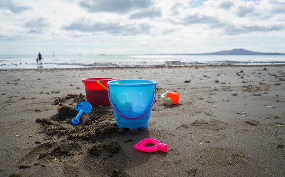 Colourful buckets and beach sand toys on the beach. Unrecognizable people playing on Milford Beach. Auckland. - Powered by Adobe