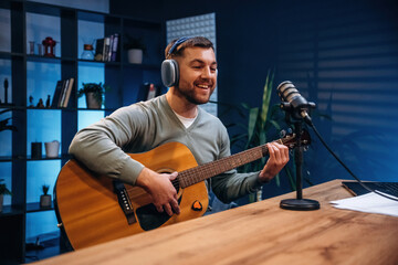 Obraz premium In headphones, playing guitar. Man with microphone in the studio, conception of podcast
