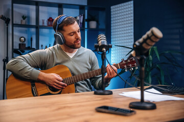 In headphones, playing guitar. Man with microphone in the studio, conception of podcast