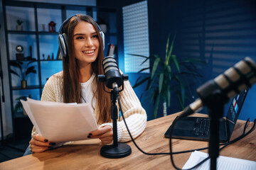 Front view, sitting. Woman is hosting radio podcast with microphone and laptop