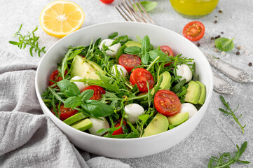 Fresh salad with arugula, mozzarella, tomatoes and avocado in a bowl. Healthy vegetarian dish.