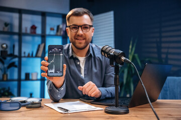 Showing graphs on the smartphone. Man with microphone in the studio, conception of podcast