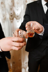 Three people in suits hold glasses with an amber-colored drink in their hands.