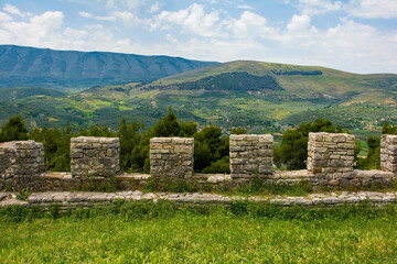 A view from the fortified walls of the 13th century Berat Castle in Albania. A picturesque rural landscape of pine trees, fields and green hills, with the Shpirag Mountain Range left