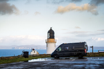 Black campervan parked at Dunnet Head Lighthouse under a clouded sunrise sky in Scotland, Europe
