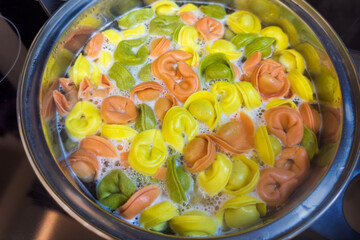 Multicolored meat dumplings during boiling in pot on a stove