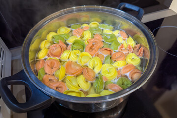 Multicolored meat dumplings during boiling in pot on a stove