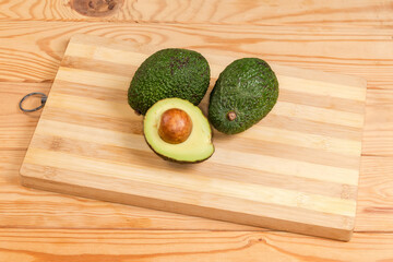 Whole and halved avocado on cutting board on rustic table