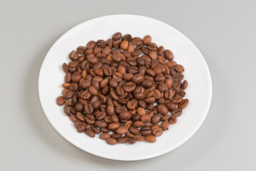 Roasted coffee beans on a white dish on gray background