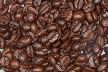 Layer of dark roasted coffee beans on a white surface