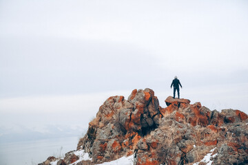 Fototapeta premium A man stands on the top of a cliff. A traveler stands on the top of a mountain and looks at the sea. Beautiful documentary landscape. Beautiful nature with a rocky mountain and a lake