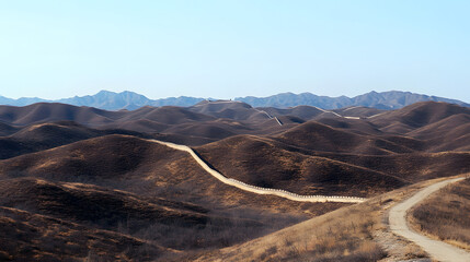 Naklejka premium Winding dirt road through mountainous terrain, serene landscape under clear blue sky, perfect for nature exploration or travel themes.