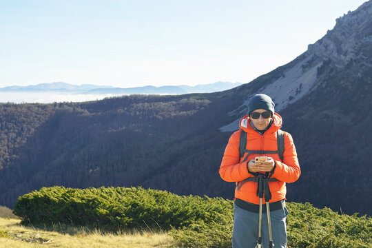 Orientation in nature using an application on a smartphone: portrait of a male tourist standing against the backdrop of mountains and checking the route on his phone. Hiker in Komovi, Montenegro.