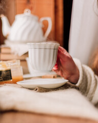 woman drinking tea from a white cup and saucer near the window, tea with honey, cozy composition, tea party by candlelight