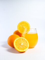 Fresh orange juice in a glass with whole and sliced oranges on a white background