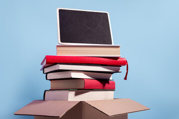 Books in a box ready for donation on blue with empty sign for text, copy space. Concept of books donations