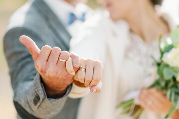 A romantic close-up of a bride and groom linking pinky fingers, showcasing their wedding rings in...