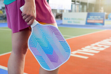 Close-up of female athlete's hand holding pickleball racket on sunny summer day. Sports played with rackets.