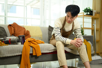 Obraz premium Exhausted man resting on the couch after cleaning with scattered clothes