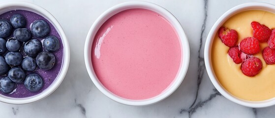 Naklejka premium Three bowls of different types of smoothies on a white marble countertop. on the left, there is a bowl of blueberries on the left side of the image.