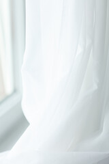 Soft, sheer white curtain lightly filters sunlight, creating a serene and airy ambiance in the room, emphasizing gentle movement and tranquility.