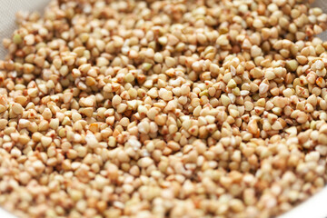 Close-up on a pile of raw buckwheat grains. The grains are light brown with darker spots, perfect for a healthy meal.