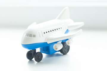 A miniature toy airplane with blue and white colors sits on a bright white surface, reflecting light, wheels down.