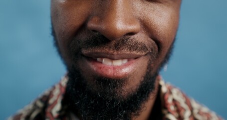 Obraz premium A bearded man with an earring in his ear, smiling standing on a blue background in the studio, close-up of his mouth