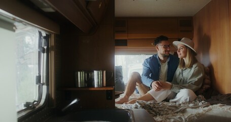 A man and a woman are talking and smiling sitting on a bed in a RV. Romantic van ride