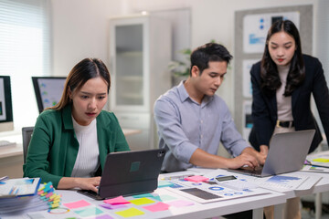 A woman is typing on a laptop in front of a man and a woman