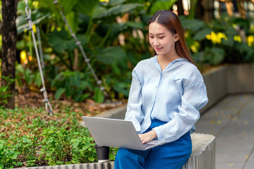 Young Asian Woman Using Laptop While Taking a Coffee Break Outdoors a Modern Urban Greenery Office Settings