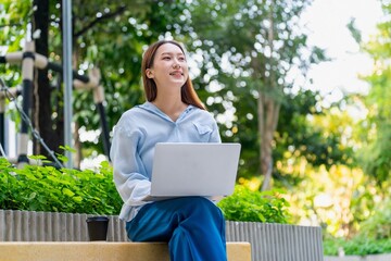 Young Asian Woman Using Laptop While Taking a Coffee Break Outdoors a Modern Urban Greenery Office Settings