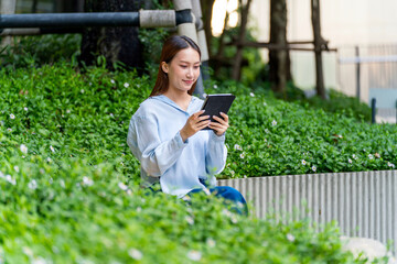 Young Asian Businesswoman In Casual Business Outfit Using Tablet Outdoors Sitting In Front a Modern Office Building