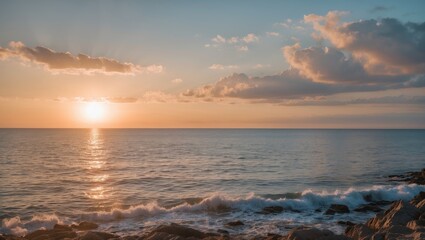 Sunset over calm ocean waters with soft waves and clouds in the sky reflecting warm light on the horizon with rocky shoreline.