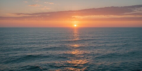 Fototapeta premium Sunset over calm ocean waters with reflections and soft cloud coverage in the sky creating a tranquil atmosphere.