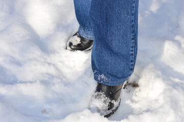 winter-themed close-up person standing in the snow blue jeans black shoes snow sticking to the...