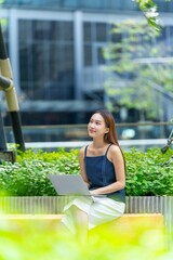 Young Asian Woman In Casual Business Outfit Using Laptop  Outdoors a Modern Office Building