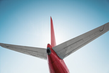 Low angle view of a tail of a red airplane. Backlit shot of airplane tail assembly - empennage of commercial airpane. © andrbk